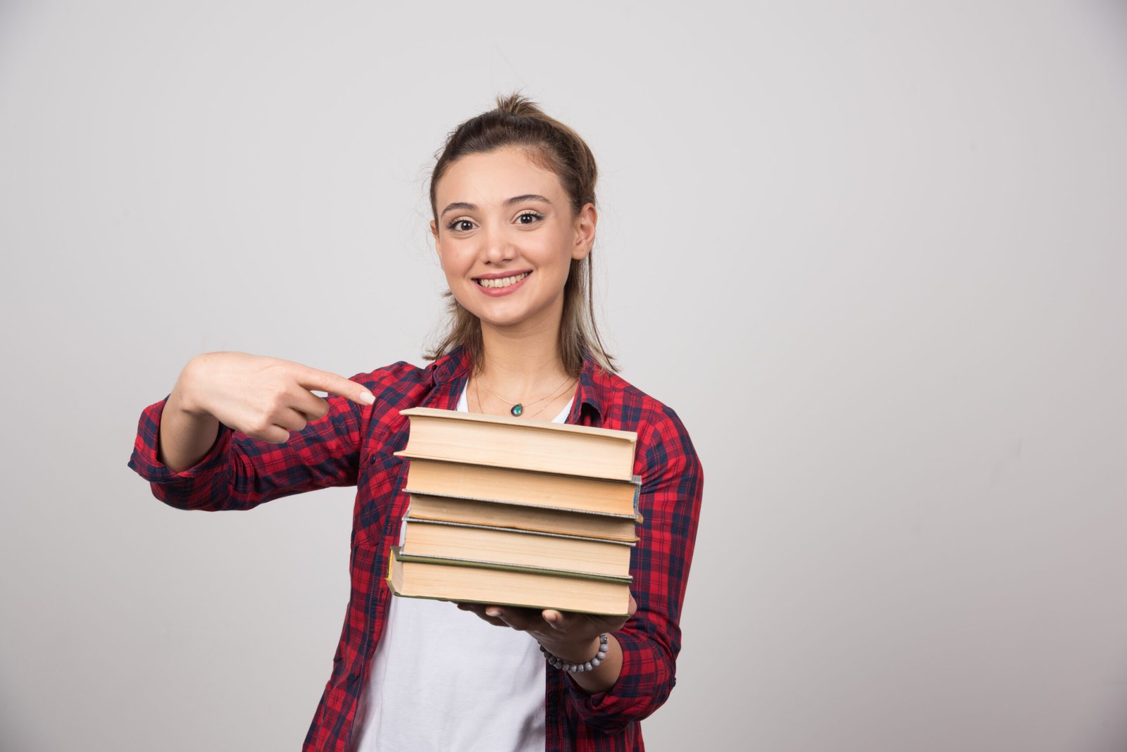 A smiling woman pointing at a stack of books